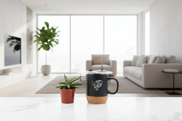 Black mug with cork base and plant design next to a small potted plant on a white surface.